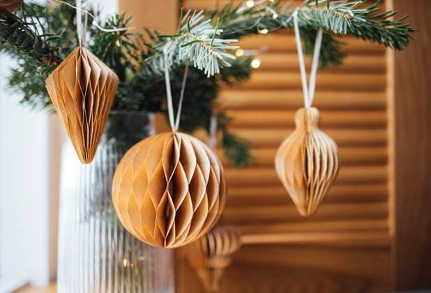 Dekorative wabenförmige Papierornamente in warmen Farbtönen, die an einem Tannenzweig hängen und mit einem hölzernen Hintergrund und sanfter Beleuchtung eine gemütliche Urlaubsatmosphäre schaffen Honeycomb paper ornaments in various shapes hang from a pine branch, enhancing a warm and inviting holiday ambiance with natural textures and soft lighting (License=RF) Copyright: xZoonar.com DashaxPetrenkox 24080791