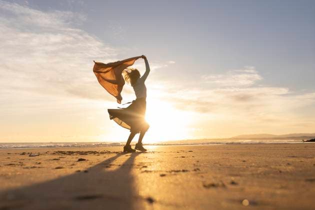 A woman stands on a beach with a scarf around her neck A woman stands on a beach with a scarf around her neck. The sky is a beautiful orange color, and the sun is setting. The woman is enjoying the moment and the beautiful scenery, 60897446.jpg RECORD DATE NOT STATED