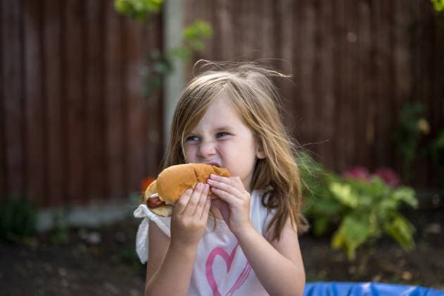 IMAGO Creative, Lifestyle, Feste im Garten #2 Child eating hot dog outdoors in summer garden barbecue party model released, Symbolfoto property released, IGEF00072