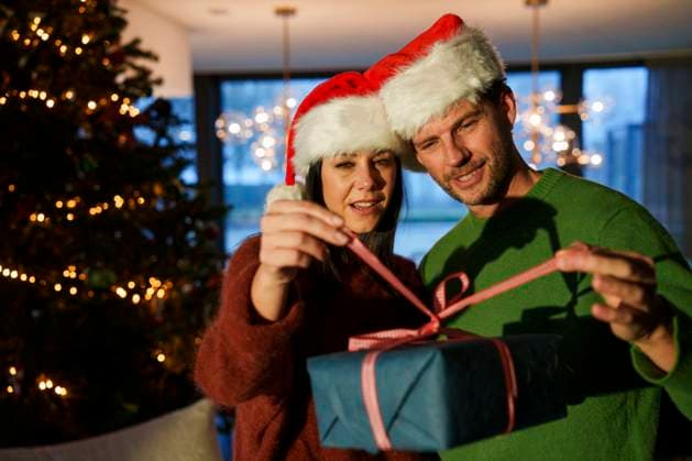 Couple exchanging a Christmas gift wearing Santa hats at home model released, Symbolfoto property released, JOSEF26927