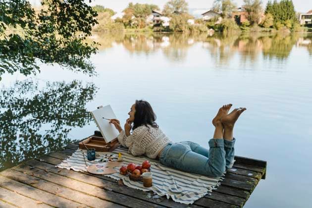 Person painting and relaxing on dock by scenic lake outdoors model released, Symbolfoto, NDEF02897