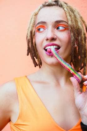 Smiling woman with dreadlocks and orange makeup enjoying rainbow candy model released, Symbolfoto, SVCF00507
