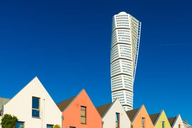 Malmo - Oktober 2018, Schweden: Blick auf den drehenden Torso Wolkenkratzer mit blauem Himmel auf den Hintergrund und eine Reihe von farbigen Wohnhäusern vor Malmo - October 2018, Sweden: View of The Turning Torso skyscraper with blue sky on the background and a row of colored residential houses in front (License=RF) Copyright: xZoonar.com RomanxSmirnovx 24141133