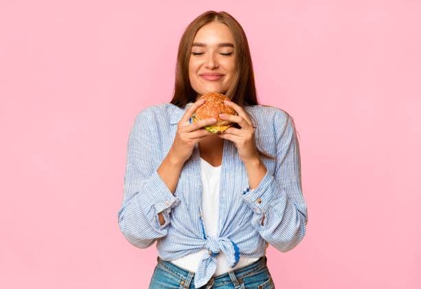 Cheerful Woman Smelling Burger Standing Over Yellow Background Junk Food. Cheerful Woman Smelling Burger Standing Over Yellow Background. Studio Shot, model released, , 61214486.jpg RECORD DATE NOT STATED
