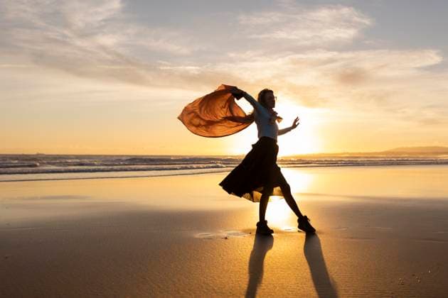 A woman is dancing on the beach with a scarf in her hand A woman is dancing on the beach with a scarf in her hand. The sky is orange and the sun is setting, model released, , 60777262.jpg RECORD DATE NOT STATED