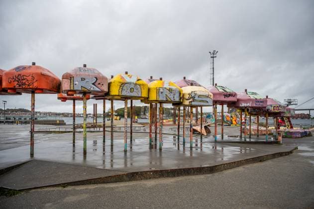 IMAGO Creative, Jahreszeit Sommer, Regen, Sommerregen Eine Reihe bunter, mit Graffiti beschmierter Regenschirme mit der Aufschrift ROONS steht in einem verlassenen Hafengebiet unter einem bewölkten Himmel, Stavanger, Norwegen A row of colorful, graffiti-covered umbrellas spelling ROONS stands in an abandoned waterfront area under a cloudy sky, Stavanger, Norway (License=RM) Copyright: xZoonar.com MarkusxBeckx 24214048