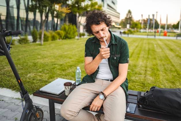 Man with curly hair sits on a park bench, lights a cigar and rests Man with curly hair sits on a park bench, lights a cigar and rests after riding an electric scooter, model released, , 62049348.jpg RECORD DATE NOT STATED