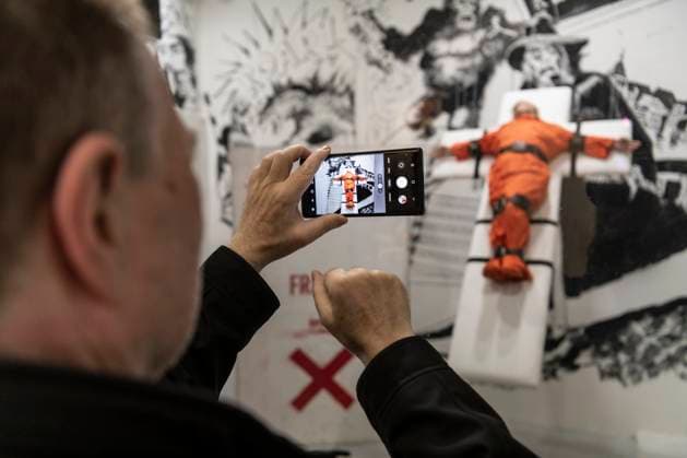 November 8, 2025, Basel, Basel-Stadt, Switzerland: A man takes a picture to a sculpture depicting the US President Donald Trump in a prisoner orange jumpsuit and strapped to a cross looking like a death row strapped-down bed, is displayed in a gallery of the city centre of Basel, Switzerland Basel Switzerland - ZUMAp199 20251108_zip_p199_005 Copyright: xMatteoxPlacuccix