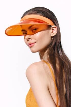 Young woman wearing an orange visor, showcasing her playful smile and confidence against a clean white background, perfect for summer fashion concepts. Stylish young woman in an orange visor exuding confidence and summer vibes, ideal for fashion and lifestyle themes, set against a minimalist white background., model released, , 98075224.jpg RECORD DATE NOT STATED