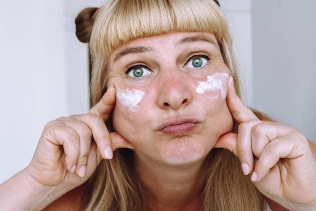 Attraktive blauäugige blonde Frau mittleren Alters mit gebundenen Pferdeschwänzen auf den Haaren, schaut in den Spiegel im Badezimmer, trägt Creme gegen Falten und Altersflecken auf, hellt das Gesicht auf Attractive blue-eyed middle-aged blonde woman, with tied ponytails on hair, looks in mirror in bathroom, applies cream against wrinkles, age spots, whitens face Copyright: imageBROKER LarysaxStefaniuk ibxiqx15576183.jpg ,model released, Symbolfoto ,property released