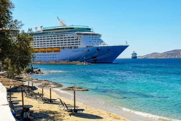 Mykonos, Kykladen, Griechenland - Kreuzfahrtschiff Voyager of the Seas liegt in der Hafenbucht Mykonos. Vorne Strandliegen und Sonnenschirme am Sandstrand Paralia Agios Stefanos. Mykonos Mykonos Griechenland *** Mykonos, Cyclades, Greece Cruise ship Voyager of the Seas moored in Mykonos harbor bay Beach chairs and umbrellas in front on the sandy beach Paralia Agios Stefanos Mykonos Mykonos Greece