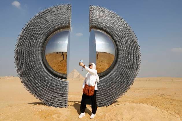 (251112) -- BEIJING, Nov. 12, 2025 -- A visitor takes a selfie in front of an artwork exhibited during the Forever Is Now international art exhibition at Giza Pyramids scenic spot in Giza, Egypt, Nov. 11, 2025. The fifth edition of Forever Is Now international art exhibition on Tuesday kicked off in the area of Egypt s Giza Pyramids scenic spot, showcasing 10 artworks of artists from different countries. The exhibition runs from Nov. 11 to Dec. 6. Ahmed Gomaa) XINHUA PHOTOS OF THE DAY AixHamaide¡¤gema 