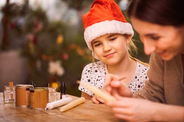 Ein kleines Mädchen mit einer roten Weihnachtsmütze sitzt an einem Tisch und sieht seine Schwester an, die Kerzen dekoriert. Ein Kind und ein Teenager basteln Weihnachtsgeschenke. A little girl in a red Christmas hat sits at a table and looks at a sister who decorates candles. A child and a teenager make Christmas gifts. Family creativity and preparation for the holiday (License=RM) ,model released, Symbolfoto Copyright: xZoonar.com DashaxPetrenkox 24226941 ,model released, Symbolfoto ,property released