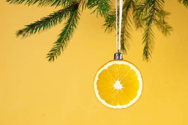 Kreative Weihnachtsdekoration: Orangenscheibe als Ornament an einem Tannenzweig mit gelbem Hintergrund Creative christmas decoration: orange slice ornament hung on pine branch with yellow background. (License=RF) Copyright: xZoonar.com FedorovaxDariax 24245051