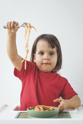 Mädchen, Kleinkind im roten Hemd, hält begeistert eine Gabel mit Spaghetti hoch, sitzt am Hochstuhl mit einer Nudelschale auf weißem Hintergrund und genießt eine verspielte und chaotische Essenszeit, vertikales Porträt Girl child toddler in red shirt enthusiastically holds up fork with spaghetti, sitting at high chair with a bowl of pasta on white background, enjoying a playful and messy mealtime, vertical portrait Copyright: imageBROKER EvgeniiaxGordeeva ibxiqx15555729.jpg ,model released, Symbolfoto ,property released