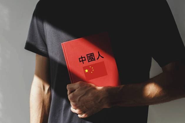 Eine Person, die ein schwarzes T Shirt trägt, hält ein rotes chinesisches Lehrbuch mit chinesischen Schriftzeichen und einer chinesischen Flagge auf dem Cover und steht im Sonnenlicht. Konzept des Sprachenlernens, Bildung, China A person wearing a black t-shirt holds a red Chinese language textbook with Chinese characters and a Chinese flag on the cover, standing in sunlight. Concept of language learning, education, China Copyright: imageBROKER EvgeniiaxGordeeva ibxiqx15555740.jpg
