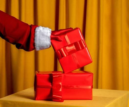 Santa hand in glove holding red Christmas present on yellow background model released, Symbolfoto, AAF00300