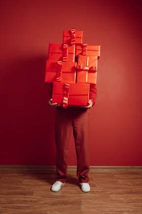 Person in red holding stacked presents against a red monochrome wall model released, Symbolfoto, AAF00330