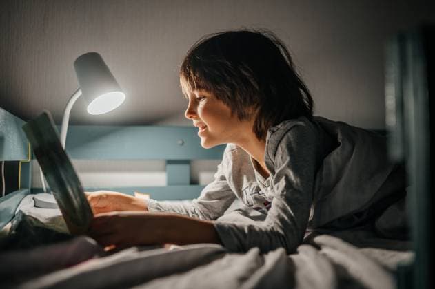 Child reading a book in bed with lamp at night in cozy bedroom model released, Symbolfoto property released, ANAF05245