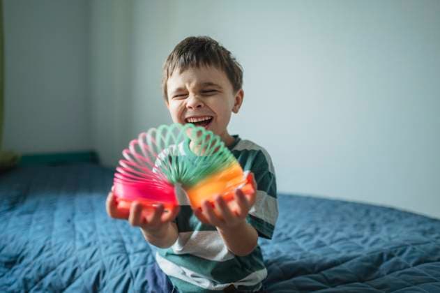 Smiling boy playing with slinky toy on bed in bright bedroom model released, Symbolfoto property released, ANAF05287