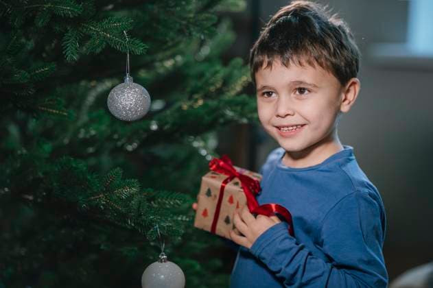 Smiling child holding Christmas present by decorated tree indoors model released, Symbolfoto property released, ANAF05309