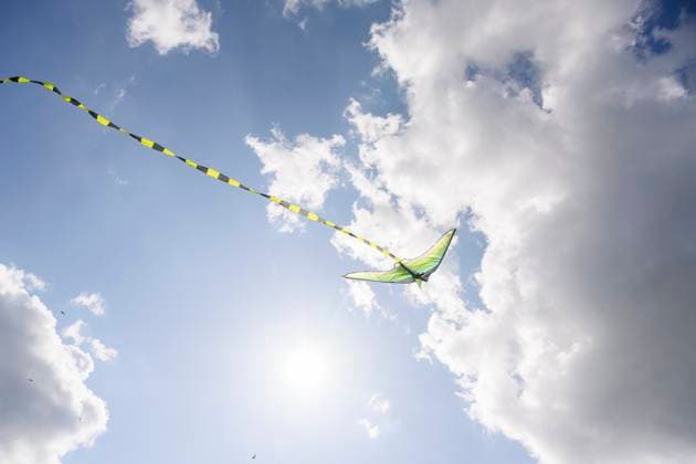 Green kite with long tail flying in blue sky with clouds and sunlight, EYAF03705