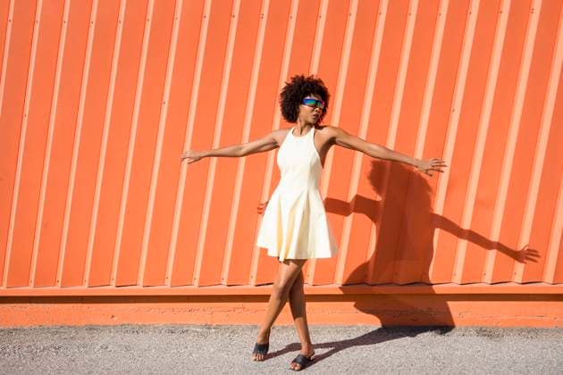 Happy woman with afro hairstyle in yellow dress dancing by orange wall model released, Symbolfoto, JSMF03464