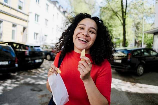 Smiling woman with curly hair enjoying sweets outdoors on sunny urban street model released, Symbolfoto, KNSF11942