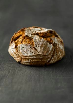 Rustic German Bauernbrot loaf on dark table with flour dusting, KSWF02389