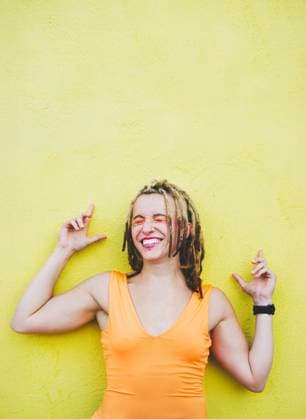Smiling woman with dreadlocks and piercings standing by yellow wall model released, Symbolfoto, SVCF00555