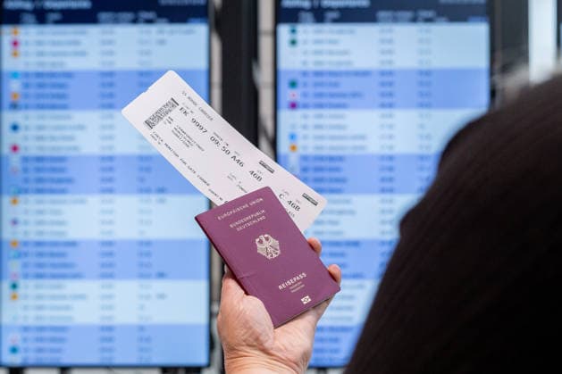Bavaria, Germany - November 25, 2025: A traveler holds her flight ticket in front of the departure board at the airport. The scene shows typical procedures for air travel from checking flight information to preparing for boarding. On the day of trial operations for the new gate in Terminal 1 at Munich Airport. *** Eine Reisende hält ihr Flugticket vor der Abflugtafel im Flughafen. Die Szene zeigt typische Abläufe einer Flugreise von der Kontrolle der Fluginformationen bis zur Vorbereitung des Boardings. Am Tag des Probebetriebs für den neuen Flugsteig im Terminal 1 des Flughafens München.