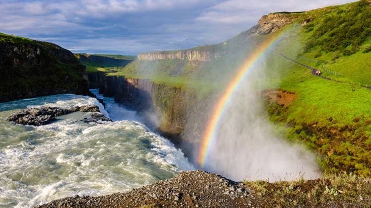 Der Wasserfall Gullfoss in Island stürzt in eine zerklüftete Schlucht, lässt Nebel in die Luft steigen und bildet einen leuchtenden Regenbogen. Üppiges Grün umgibt die dramatische Landschaft unter einem teilweise bewölkten Himmel. Gullfoss waterfall in Iceland cascades into a rugged canyon, sending mist into the air and forming a vibrant rainbow. Lush greenery surrounds the dramatic landscape under a partly cloudy sky. (License=RF) Copyright: xZoonar.com FokkexBaarssenx 24199183