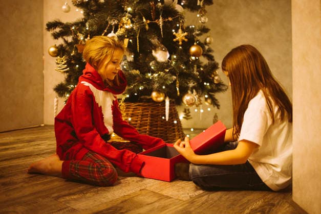 Zwei Kinder packen freudig Geschenke vor einem wunderschön geschmückten Weihnachtsbaum aus, umgeben von festlichem Schmuck und warmer Weihnachtsatmosphäre, die den Geist des Festes einfängt Children excitedly opening presents near a decorated Christmas tree, with twinkling lights and ornaments creating a joyful holiday atmosphere (License=RF) ,model released, Symbolfoto Copyright: xZoonar.com DashaxPetrenkox 24281500 ,model released, Symbolfoto ,property released