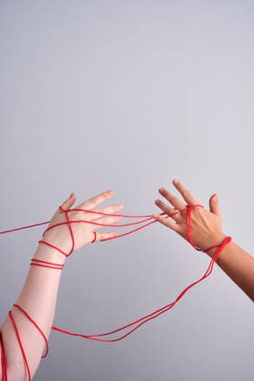 Verbundene Hände, die einen roten Faden bilden Hands entangled by a red string, symbolizing connection, destiny, and interpersonal relationships between people (License=RF) Copyright: xZoonar.com MAREVGENNAx 24305278
