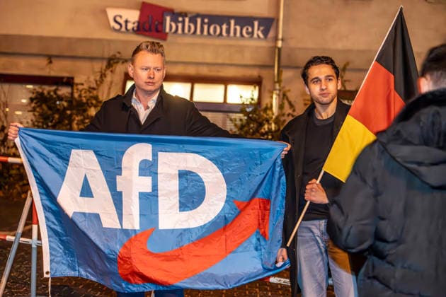 AfD Demonstranten protestieren gegen Dragqueen-Lesung für Kinder vor der Stadtbibliothek Moosach, München, 1. Dezember 2025 Deutschland, München, 1. Dezember 2025, AfD Demonstranten mit Deutschlandfahne protestieren gegen Dragqueen-Lesung für Kinder vor der Stadtbibliothek Moosach, Dragqueen Vicky Voyage macht währenddessen eine Lesung in der Stadtbibliothek Moosach, sie liest vor Familien mit Kindern aus Kinderbüchern vor, vor der Bibliothek in der Hanauer Straße kommt es während der Lesung zu heftigen Protesten von Rechtsextremen, auch eine christlich-fiundamentalistische Gruppe hatte gegen die von ihnen so genannte Frühsexualisierung von Kindern protestiert, Montagnachmittag ab 16 Uhr im Stadtteil Moosach, Bayern