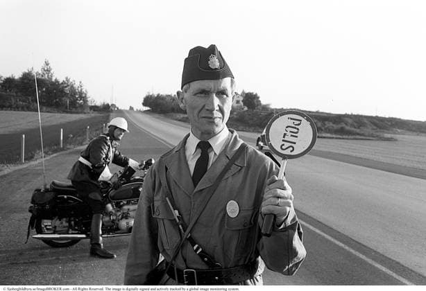 Polizeiliche Verkehrsüberwachung auf Riksettan, 1958. Zwischen 1945 und 1962 diente der Riksväg 1 als Hauptautobahn zwischen Helsingborg und Stockholm. Heute ist diese Route Teil der Europastraße E4. Ein Motorradpolizist auf einem BMW Motorrad und ein Polizist, der ein Polizeischild hält, steht am Straßenrand, überwacht aufmerksam den Verkehr und ist bereit, das nächste Auto zur Kontrolle zu stoppen. Schweden, 1958. In den 1950er Jahren, als der Autoverkehr auf dem expandierenden Straßennetz Schwedens zunahm, spielten Polizeipatrouillen eine entscheidende Rolle bei der Gewährleistung der Straßenverkehrssicherheit und der Strafverfolgung. Motorradeinheiten, die mit wendigen BMW Motorrädern ausgestattet waren, waren besonders effektiv bei de Copyright: imageBROKER Sjoberg ibljsj15797842.jpg