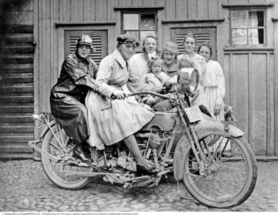 Die Kinder aus der Nachbarschaft spielen auf einem Harley Davidson Motorrad von 1922. Kinder unterschiedlichen Alters haben Spaß in einem Hinterhof in Jönköping, verkleidet und um das Motorrad versammelt. Im Hintergrund sind die Türen zu den Nebengebäuden sichtbar, die in der Vergangenheit in Höfen üblich waren The neighborhood kids are playing on a 1922 Harley-Davidson motorcycle. Children of various ages are having fun in a backyard in Jönköping, dressed up and gathered around the motorcycle. In the background, the doors to the outhouses, which were common in yards in the past, are visible Copyright: imageBROKER Sjoberg ibljsj15797847.jpg