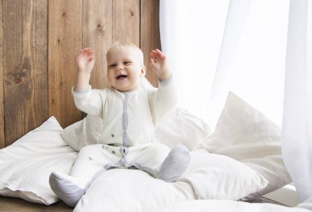 Kleinkind lächelt fröhlich und schaut weg, sitzt auf einer weißen Feder mit Kissen in der Nähe der Holzwand Toddler smiling cheerfully and looking away sitting on white feather with pillows near wooden wall Copyright: imageBROKER IuliiaxIsaeva ibxiqx15403163.jpg ,model released, Symbolfoto ,property released
