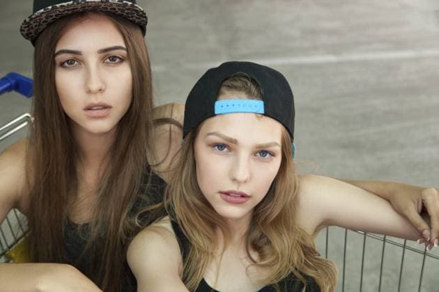 Porträt von schönen blonden und brünetten Freunden in Mützen, die in die Kamera schauen, während sie im Einkaufswagen sitzen Portrait of beautiful blonde and brunette friends in caps looking at camera while sitting in shopping cart Copyright: imageBROKER IuliiaxIsaeva ibxiqx15403857.jpg ,model released, Symbolfoto ,property released