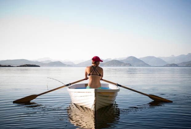 A woman rows a white boat in calm water with mountains in background Quathiaski Cove, British Columbia, Canada CR_AXTH251205-1863376-01 ,model released, Symbolfoto