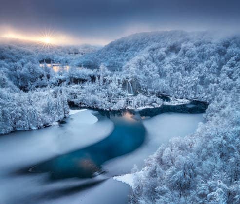Aerial drone view of frozen lakes and waterfalls surrounded by snowy forest at sunrise in Plitvice Lakes National Park, Croatia. Winter landscape with icy cascades and scenic European nature. Top view Model Released DenisBilytskyi_ID32328_1102297_003 Copyright: xx
