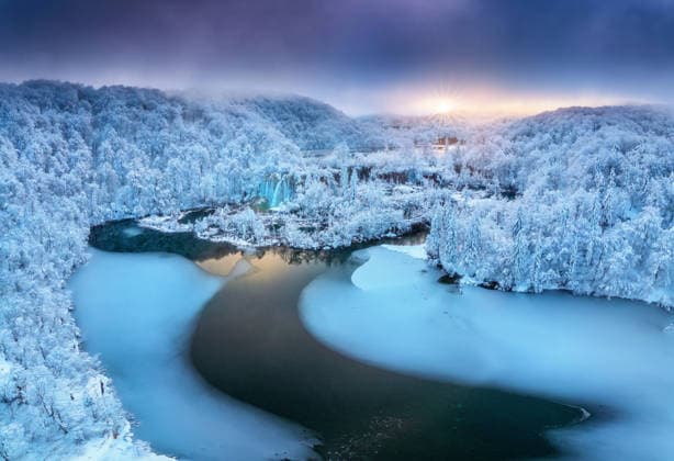 Aerial drone view of frozen lakes and waterfalls surrounded by snowy forest at sunset in Plitvice Lakes National Park, Croatia. Winter landscape with icy cascades and scenic European nature. Top view Model Released DenisBilytskyi_ID32329_1102309_002 Copyright: xx