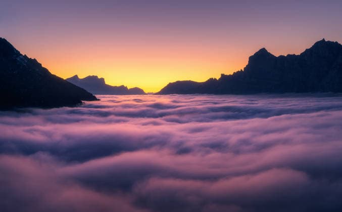 Creative Highlights World Aerial view of low clouds in the Swiss Alps with mountain silhouettes and vibrant sky and fog-filled valley at sunset. Switzerland. Top view of mountains in low pink clouds and orange sky at twilight Model Released DenisBilytskyi_ID33553_1167675_004 Copyright: xx