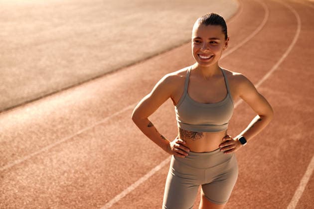 Fit confident woman posing on outdoor track in morning sunlight Strong athletic woman with tattoos standing on stadium track in activewear, hands on hips, looking confident. Concept: female empowerment, fitness, healthy lifestyle, self-confidence, morning workout. Model Released OrionProduction_ID32302_1100556_009 Copyright: xx
