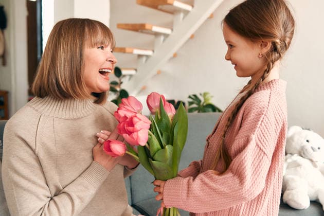 Family at home. Mom daughter and granddaughter at home. Cute child granddaughter congratulating her grandmother by giving her flowers and a gift while sitting on the sofa in the living room. Concept of Women s Day and Mother s Day. Model Released OrionProduction_ID32357_1103040_019 Copyright: xx