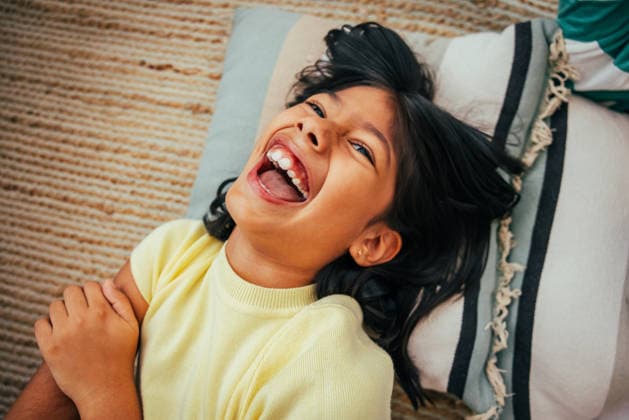 MR_ID31765_22979_AlexPelaez.jpg, MR_ID31765_22980_SarahRamirez.jpg A cheerful child with dark hair and a bright smile is lying back on a colorful pillow, radiating happiness and joy. The cozy setting adds warmth to the joyful moment Model Released AscProductions_ID31765_1080017_040 Copyright: xAscxProductionsx