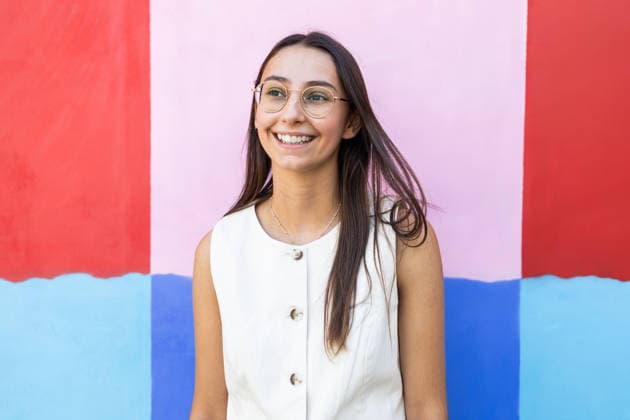 A businesswoman smiles confidently while standing against a vibrant, colorful background. She wears stylish glasses and a professional white outfit, exuding positivity and professionalism. Model Released DavidMunoz_ID31580_1073824_015 Copyright: xDavidxMunozx RECORD DATE NOT STATED