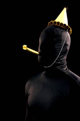 Party celebration with costume and festive hat A person in a black bodysuit celebrates with a festive gold party hat and noise maker against a dark background, capturing a unique and intriguing holiday atmosphere Model Released SergioVictorVega_ID32104_1093196_002 Copyright: xSergioxVictorxVegax RECORD DATE NOT STATED