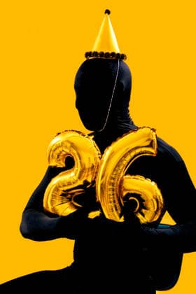 New year party celebration with golden balloons Amidst a vibrant orange backdrop, a person in a black suit holds gold balloons shaped as the number 26, symbolizing a festive New Year celebration, complete with a party hat Model Released SergioVictorVega_ID32104_1093204_005 Copyright: xSergioxVictorxVegax RECORD DATE NOT STATED