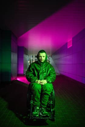 Behinderter Mann im Rollstuhl in Farbe Neon rgb Licht zum Ausdruck psychische Gesundheit Kämpfe und Krise. Pensive young disabled man in wheelchair walking alone, sitting in color neon rgb light looking at camera with tired sad expression. Male with disability showing signs of heavy mental state and apathy (License=RF) ,model released, Symbolfoto Copyright: xZoonar.com DmitriixMarchenkox 24319253 ,model released, Symbolfoto ,property released